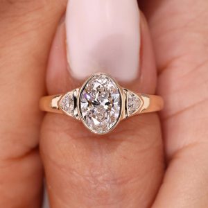 Oval bezel-set three stone engagement ring with trapezoid side accents